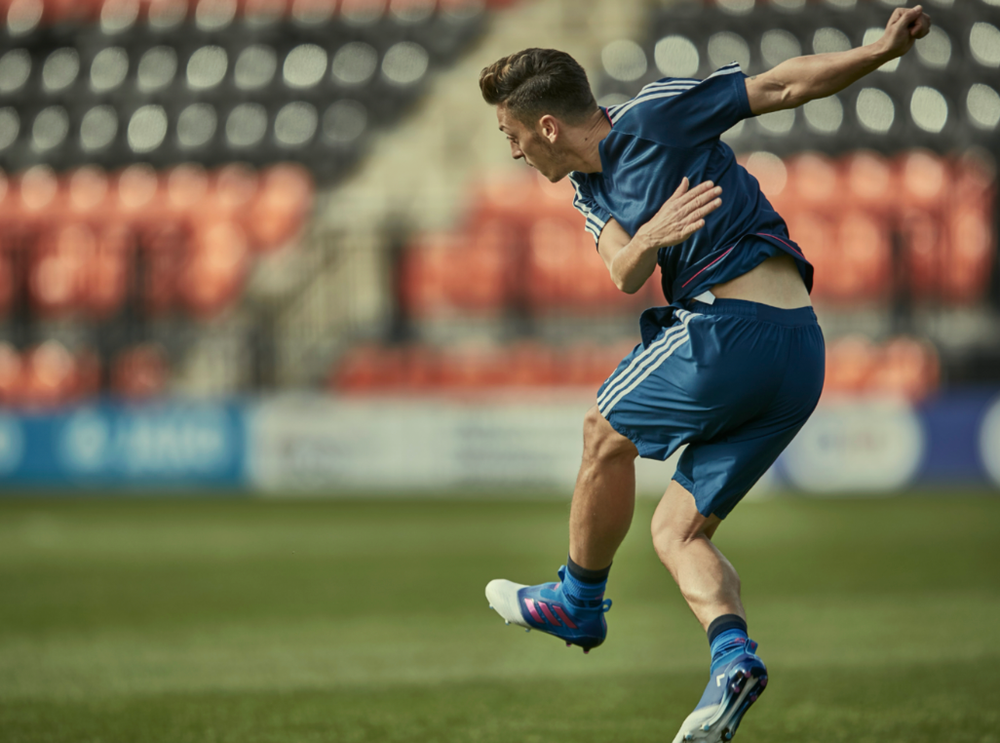 Soccer player in blue uniform kicking ball on stadium field.