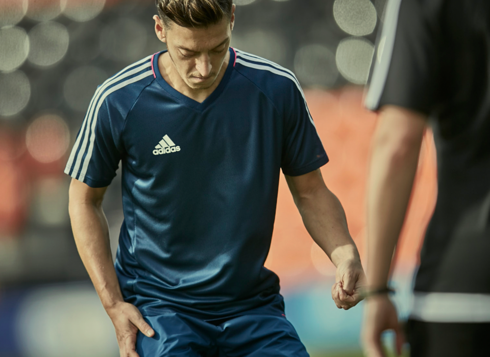 Athletes in blue Adidas jerseys training on soccer field with stadium lights in background.