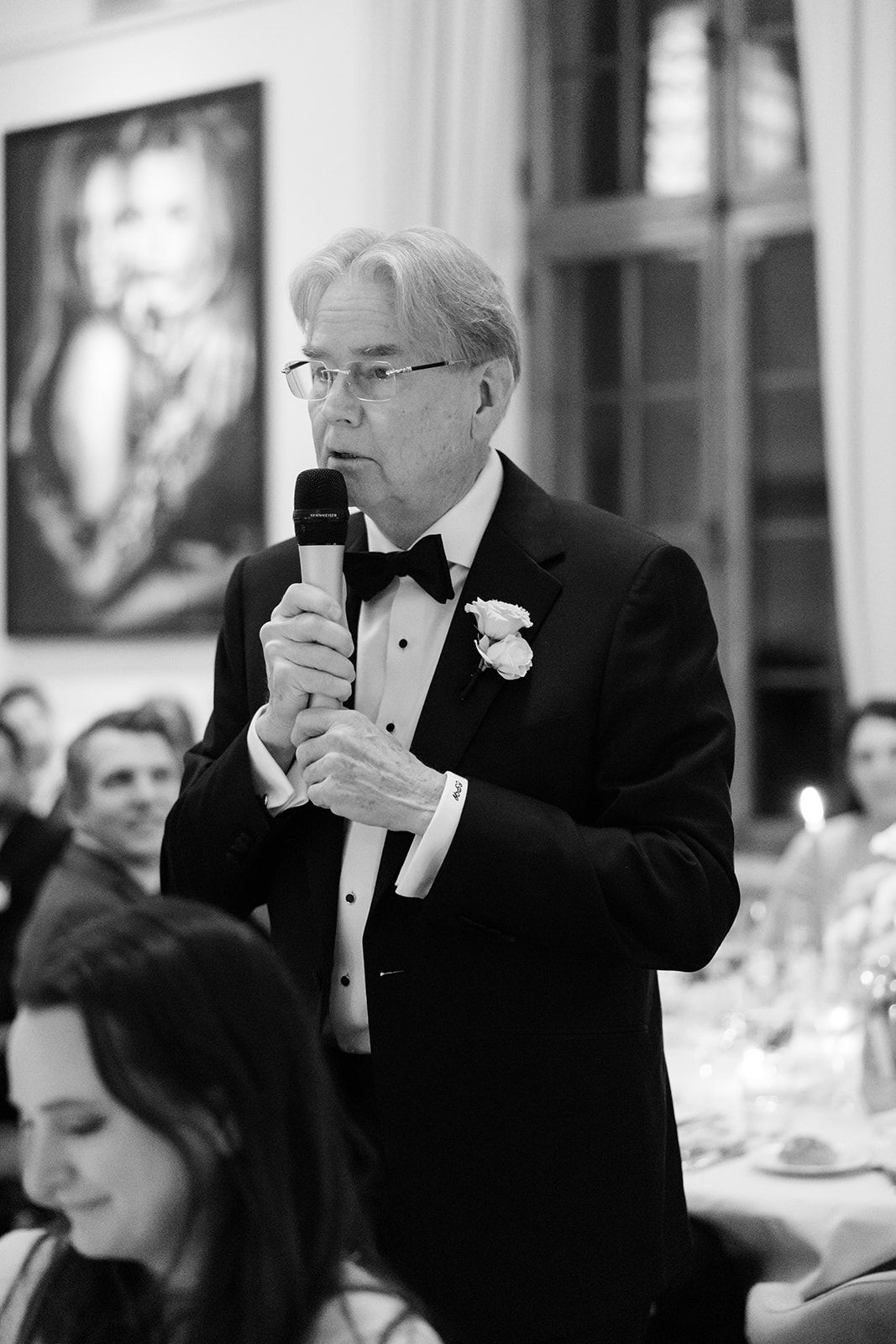 A guest in a black tuxedo takes photos with their phone during a formal event.
