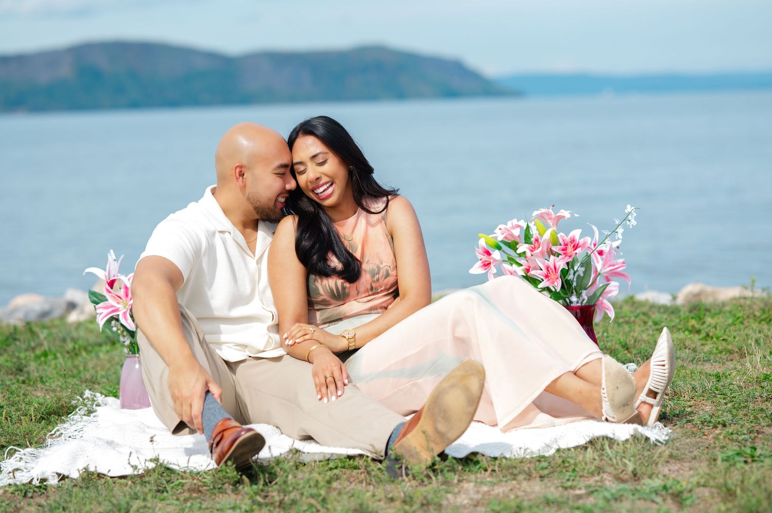 Couple in white outfits sharing romantic moments during a seaside photoshoot with ocean and hills in the background.