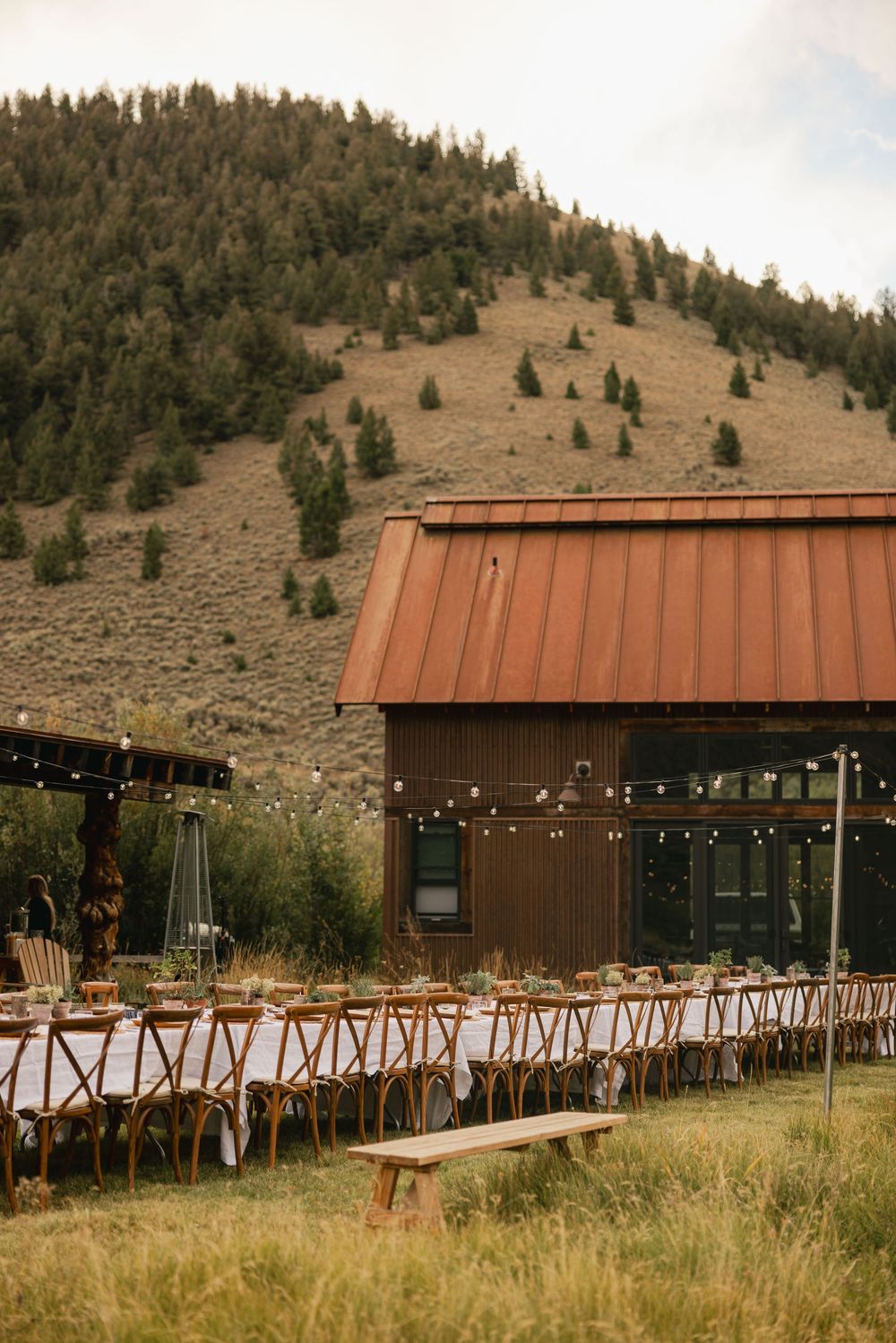 Rustic barn wedding venue with long dining tables, string lights, and a stunning mountain backdrop in a scenic outdoor setting.