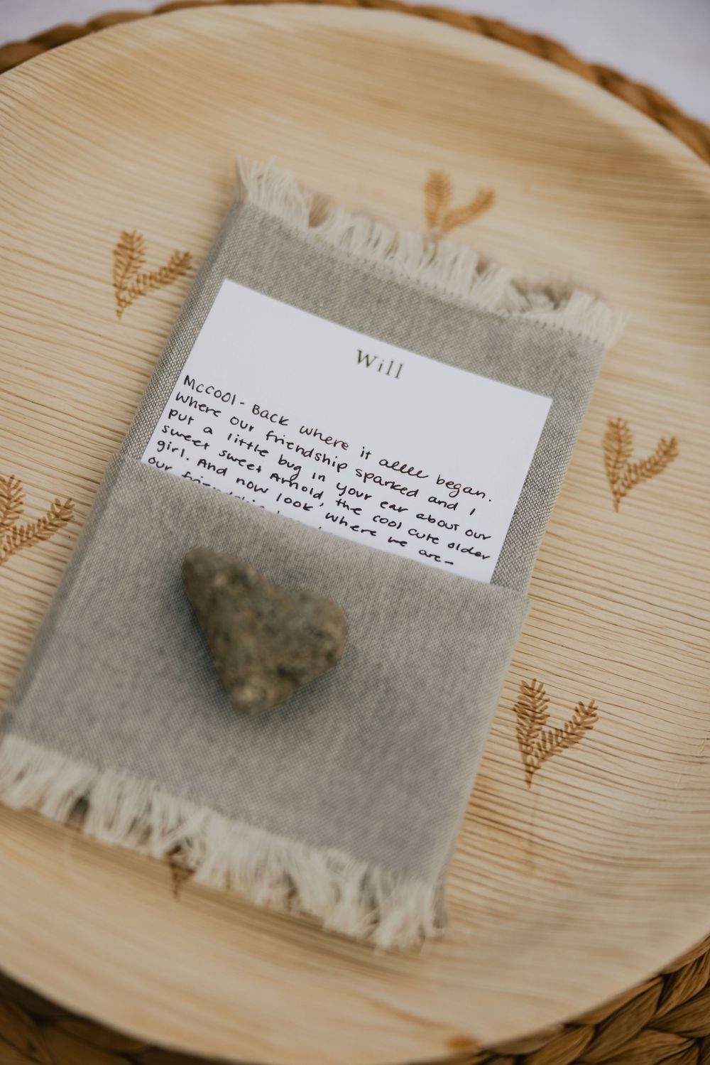 Rustic wedding vow card with handwritten note, heart-shaped stone, on linen fabric atop a wooden slice centerpiece.
