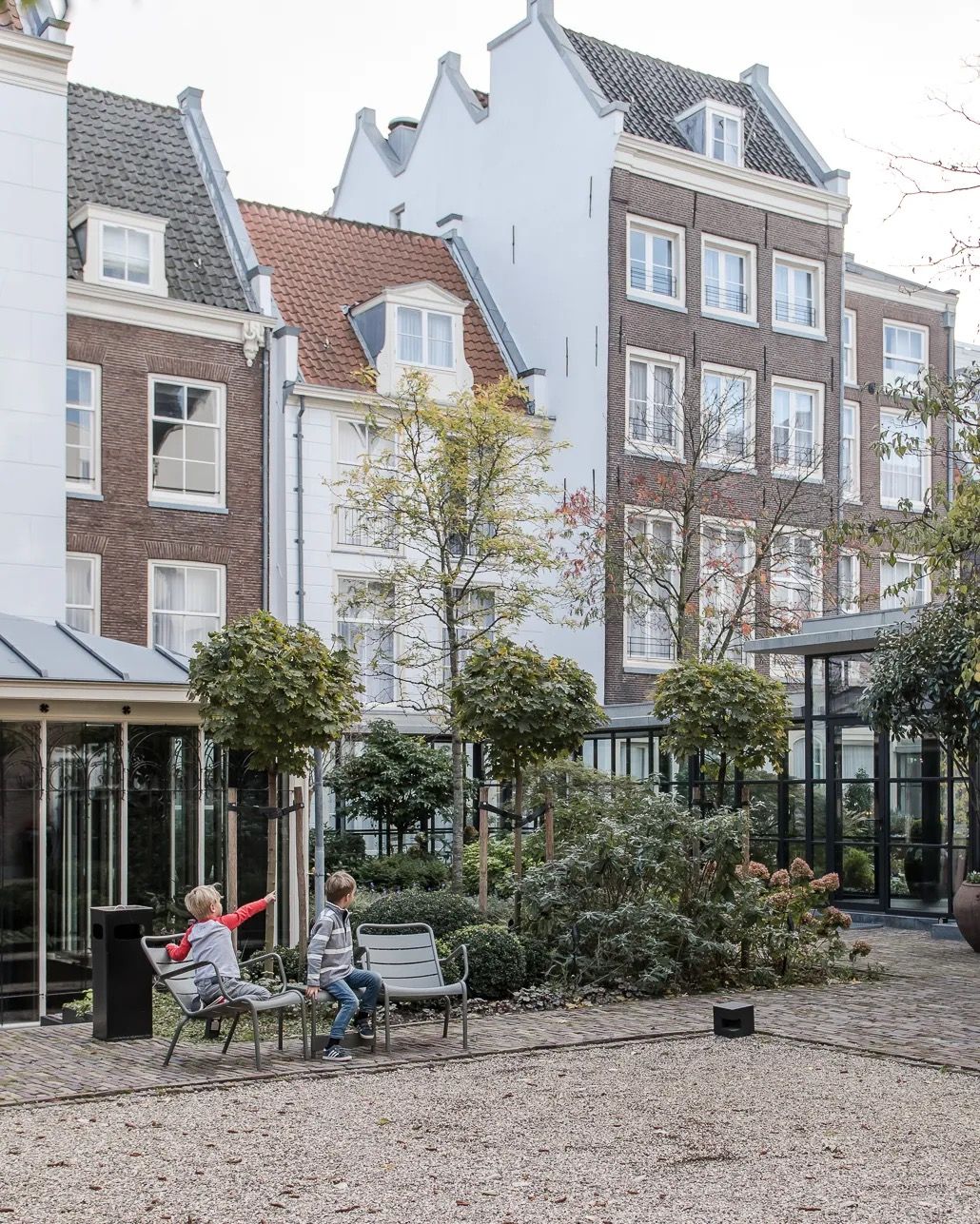 Charming Amsterdam square with brick houses, benches, and a child playing in the centre.