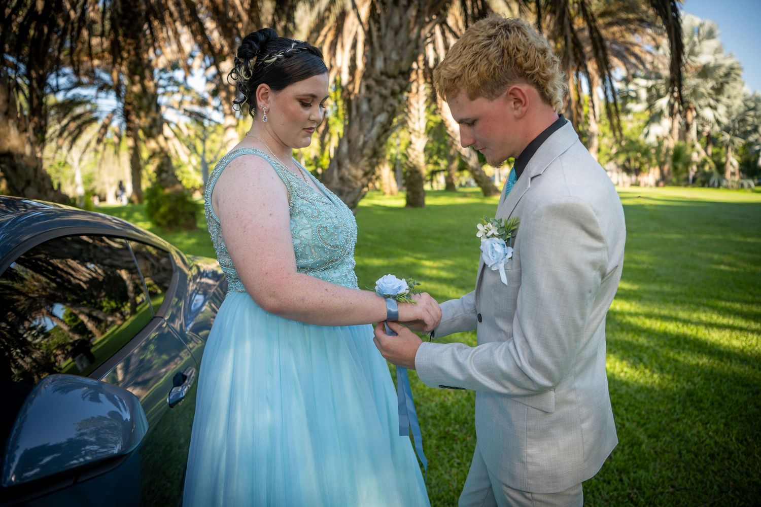 A couple shares a romantic moment in formal attire during a ceremony in a palm tree garden setting.