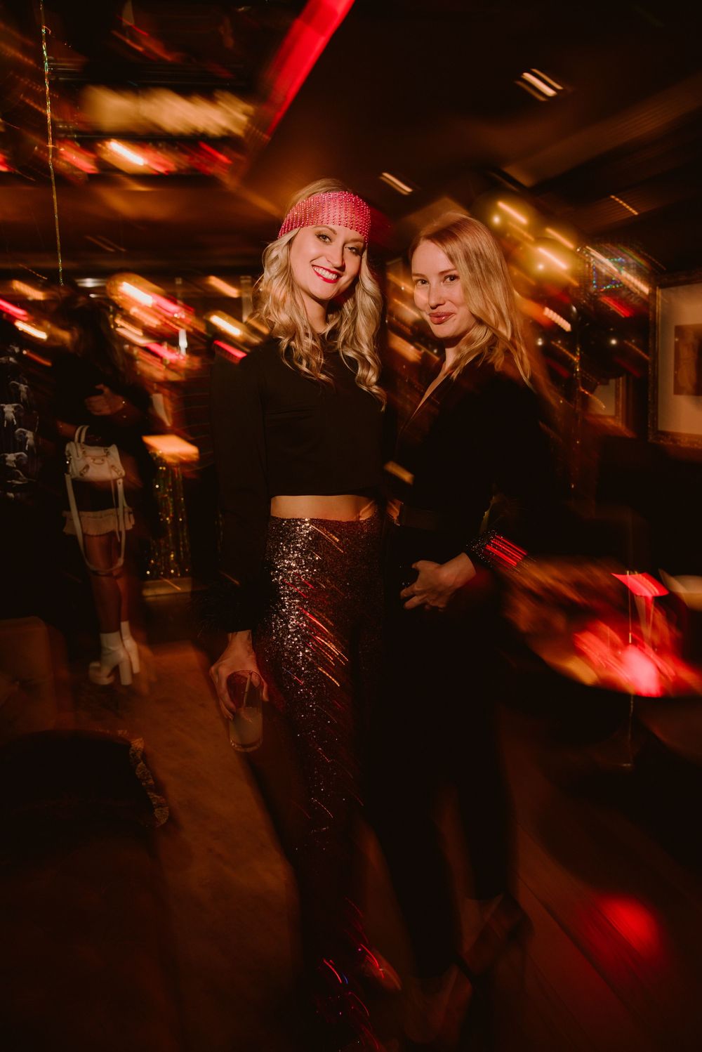 People dancing and socializing in a dimly lit nightclub with red lighting and motion blur effects.