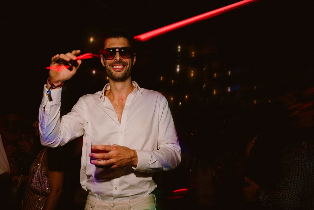 A nightclub scene with red lighting and people dancing and socializing in a dark atmosphere.
