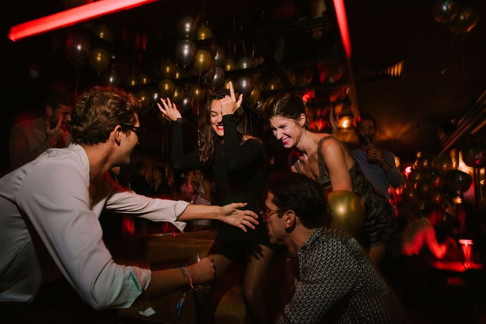 People dancing and socializing in a dimly lit nightclub with red lighting and festive atmosphere.