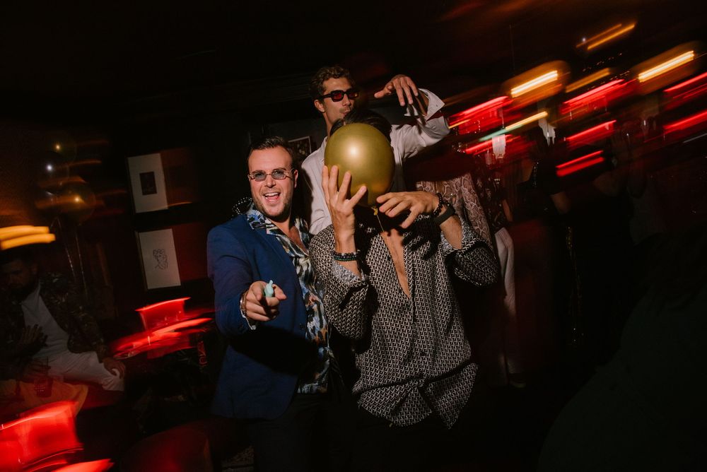 Partygoers enjoying themselves in a dark club setting with red accent lights overhead.