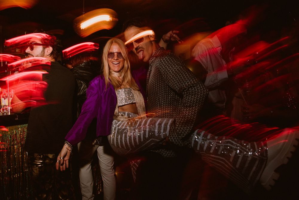 Nightclub crowd silhouetted against warm orange and red ambient lighting creating a vibrant party atmosphere.