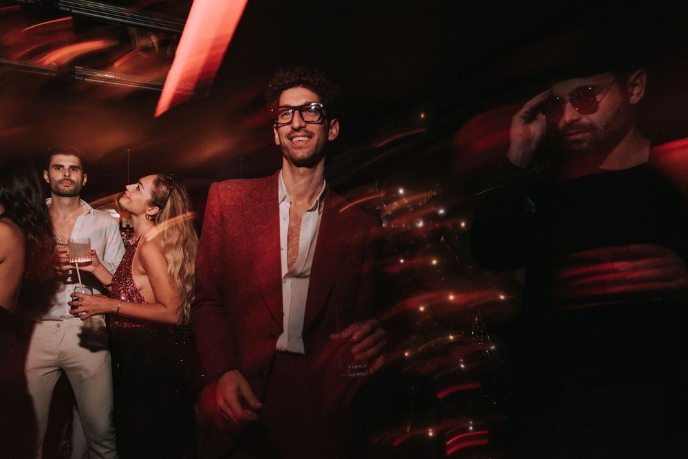 People mingling and dancing at a nightclub event with moody red lighting effects.