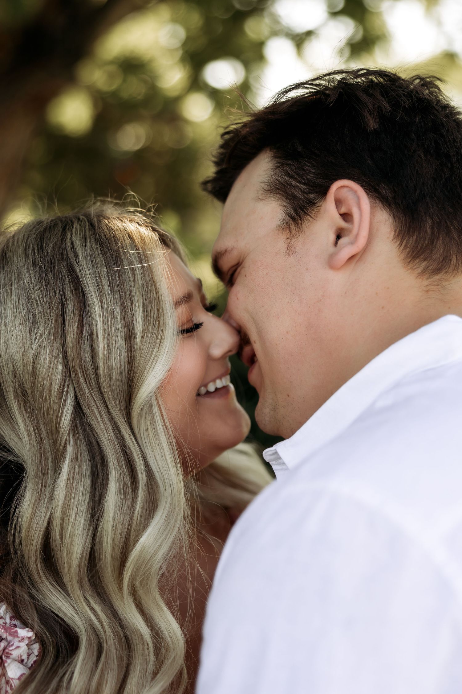 A romantic couple sharing an intimate moment in a sun-lit outdoor setting.