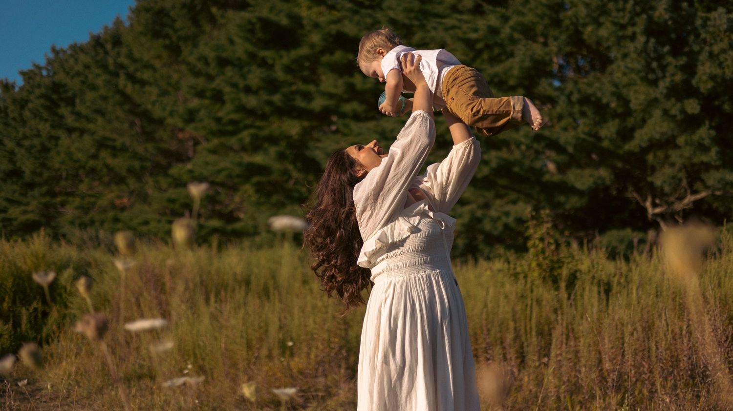 A joyful moment captured in a sunlit meadow with tall grass and evergreen trees in the background.