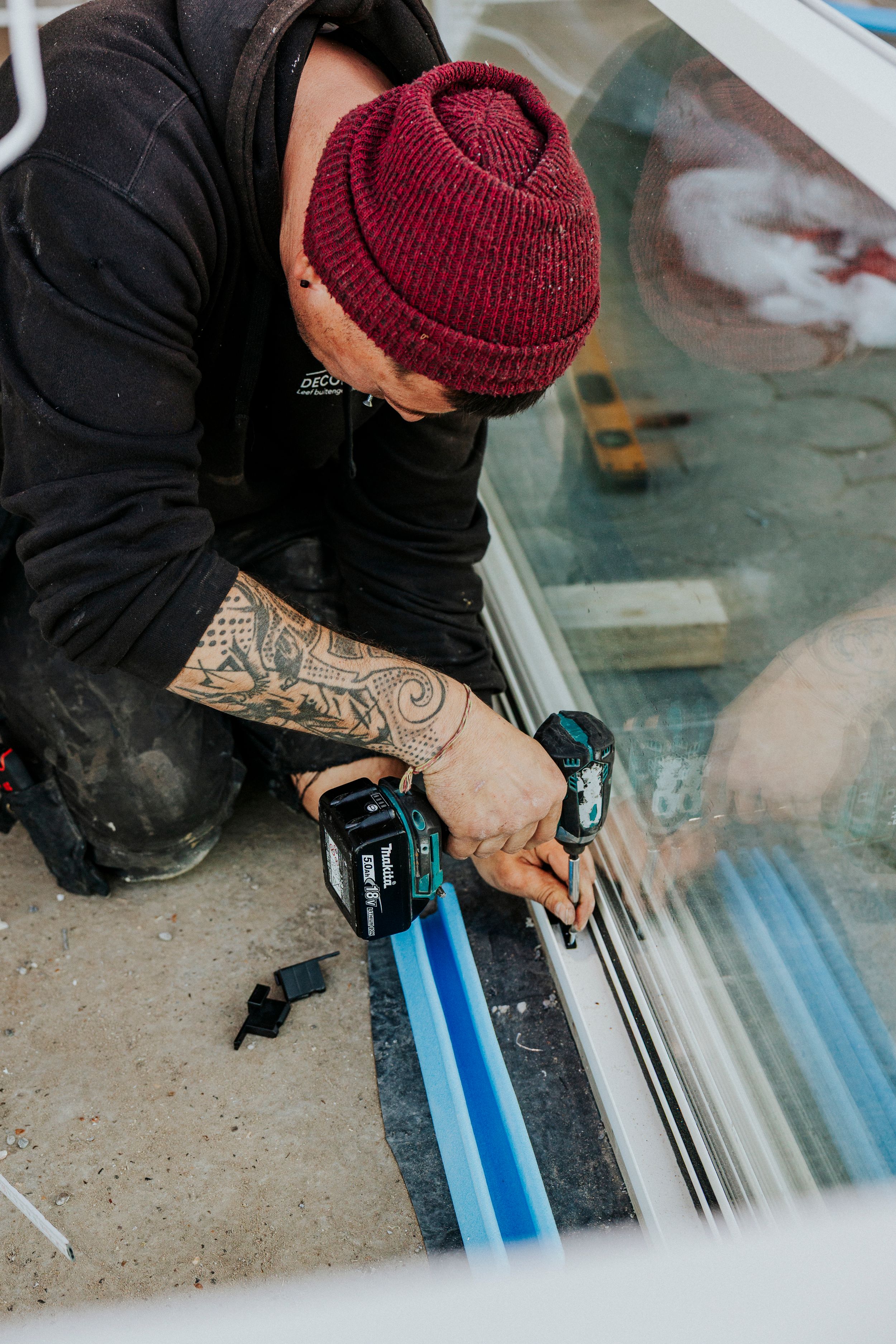 Person wearing red beanie installing floor materials during renovation.