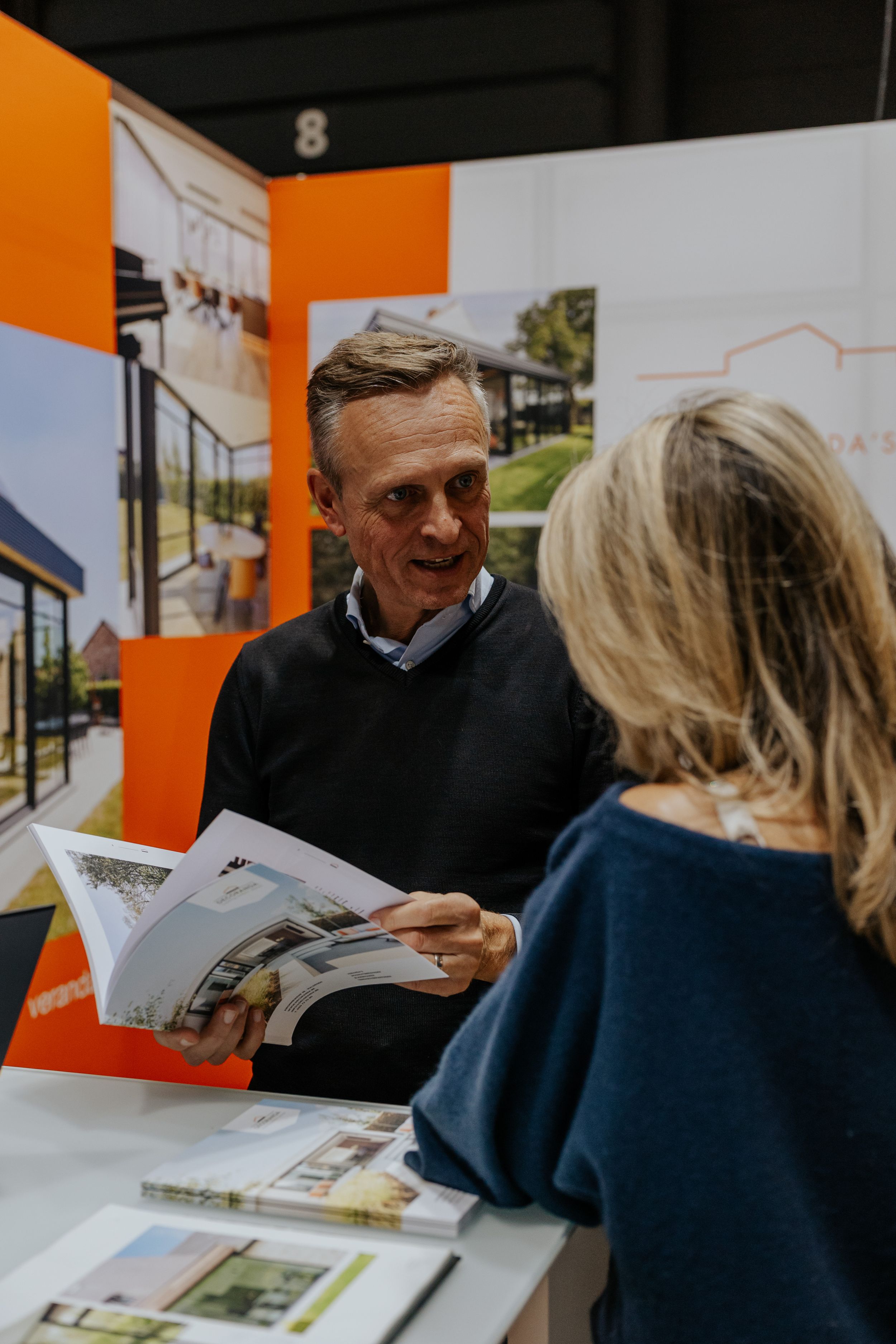 People reviewing property brochures at a consultation table with orange wall background.