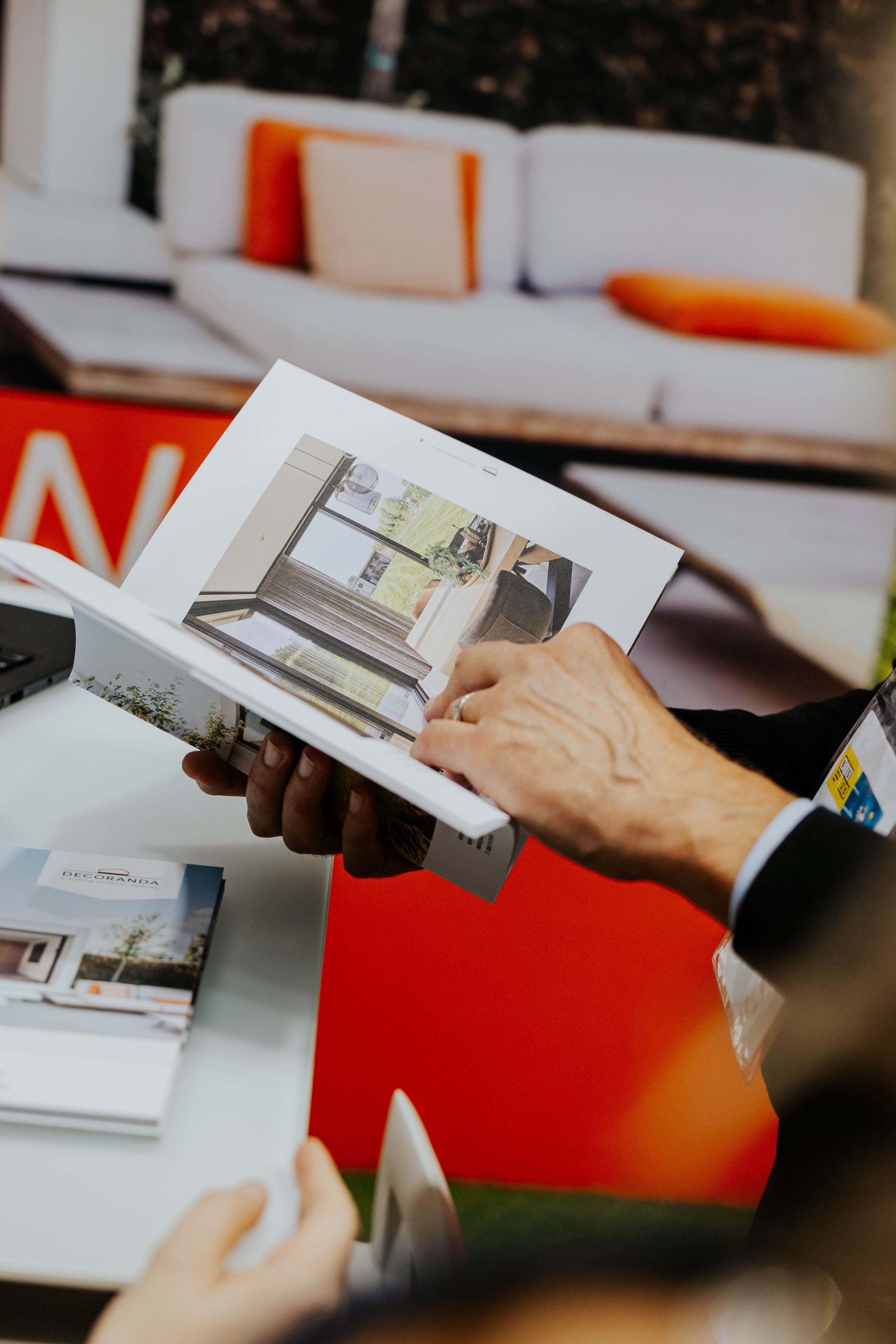 Hands flipping through architectural design brochures on white and red surface.