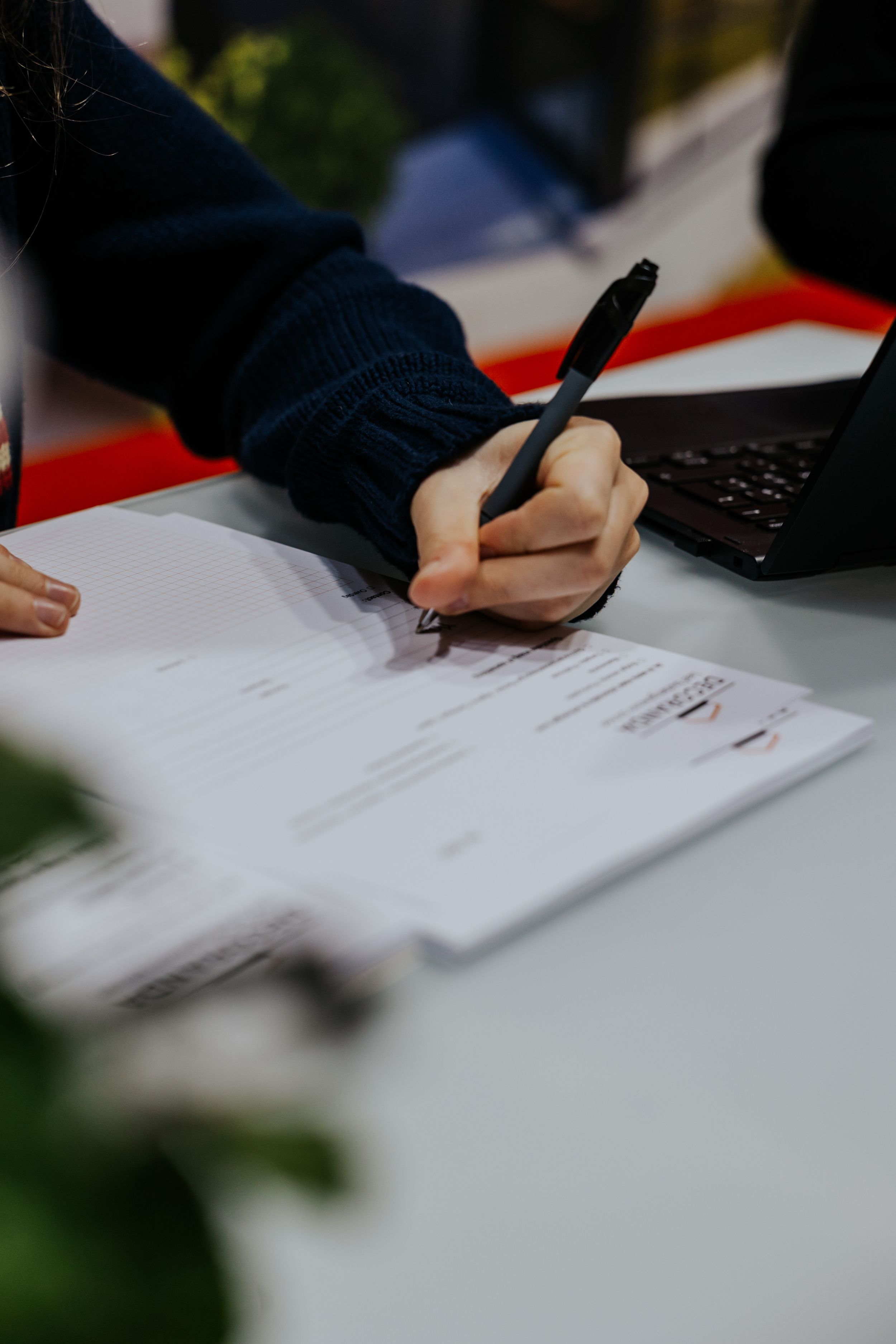 Close-up of hands signing documents on white table surface.