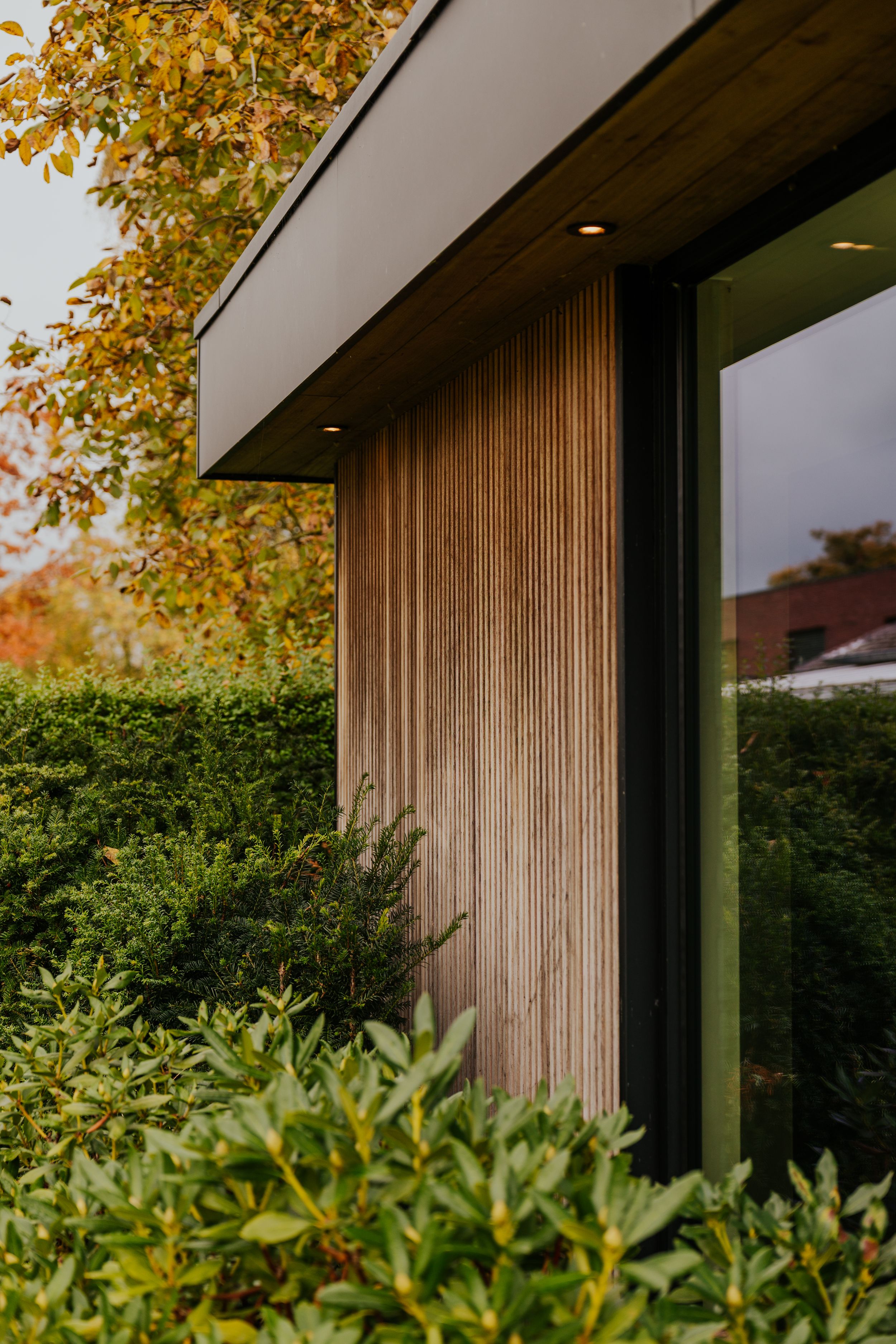 Contemporary wooden-clad building exterior with lush green landscaping and fall foliage.