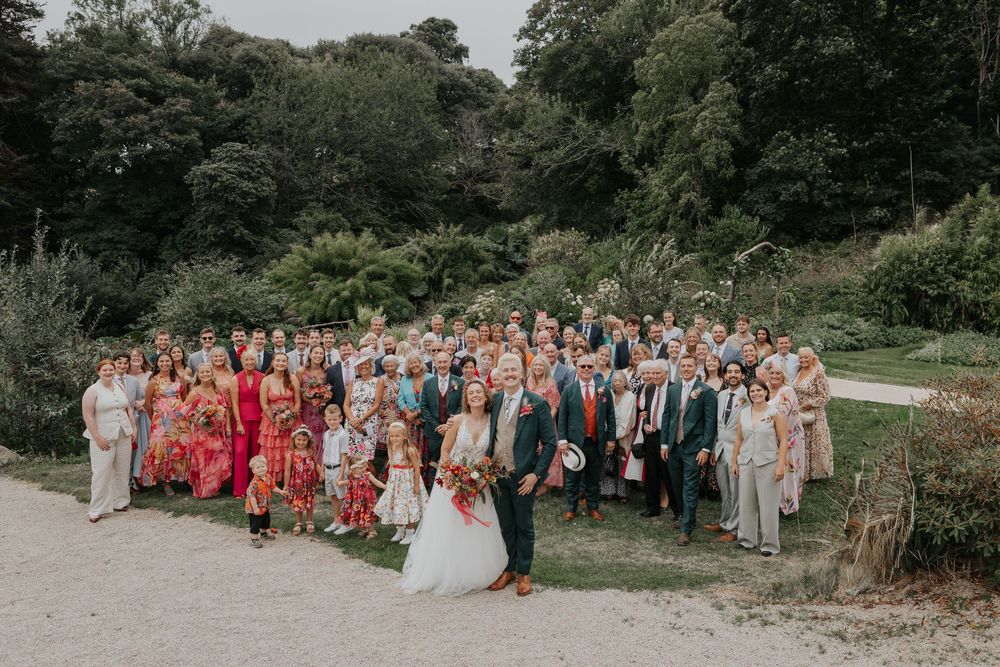 Large wedding group photo of bride, groom, and all guests gathered outdoors in garden setting.