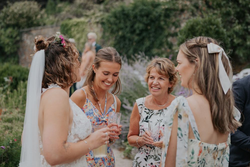 Bride in white dress shares joyful moment with three smiling women at outdoor wedding.