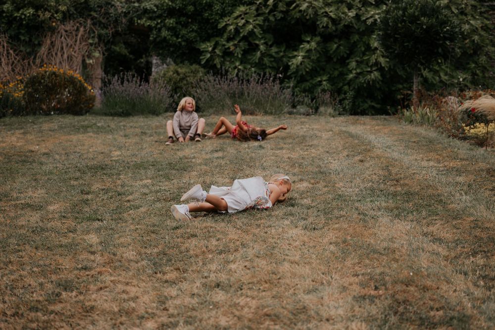 Three people relax lying on green grass in a garden at a wedding event.