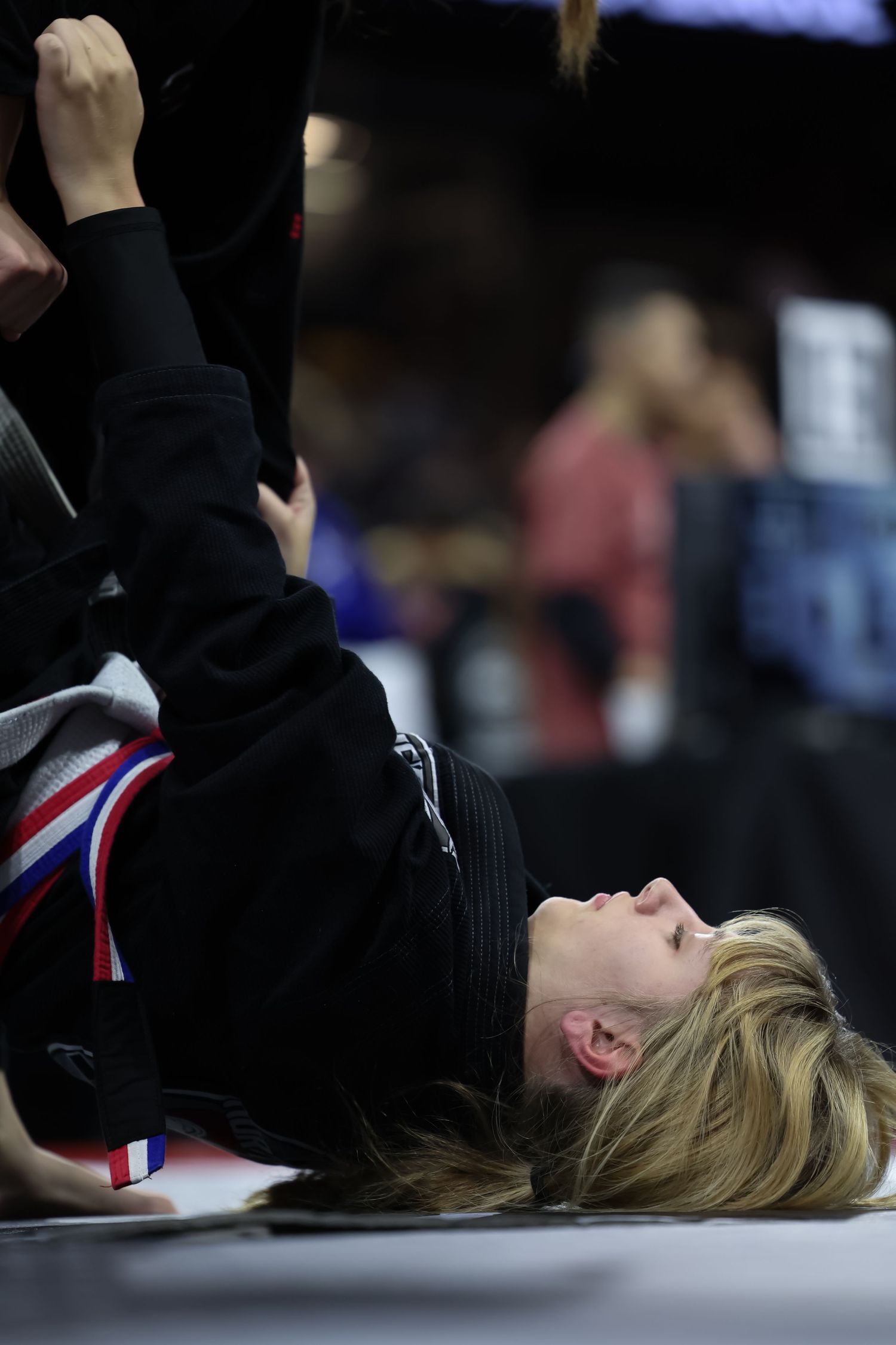 Martial artist in black uniform executing a rolling move on competition mat.