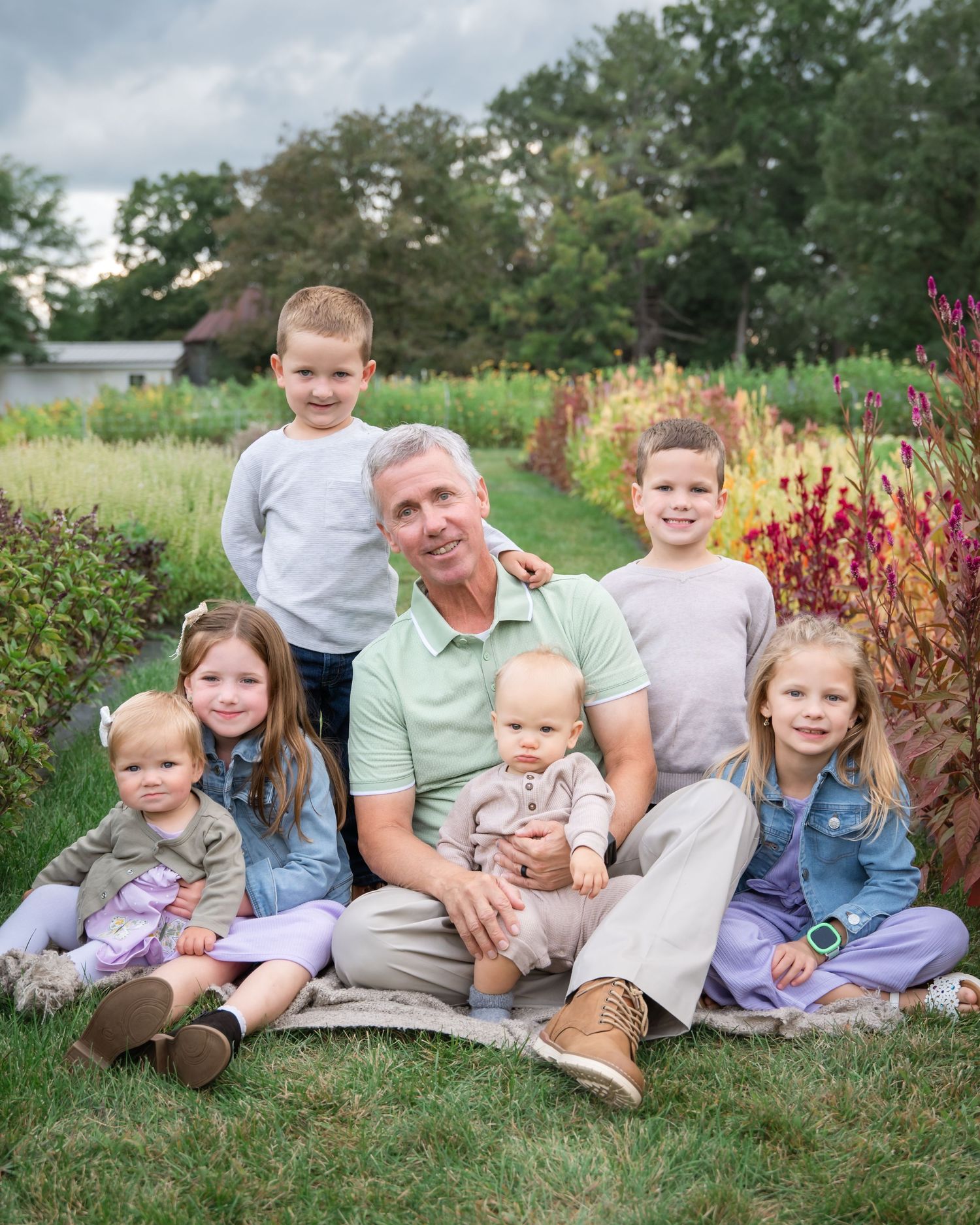 Family group lounging together on grass during outdoor photo session in park with colorful foliage in background.