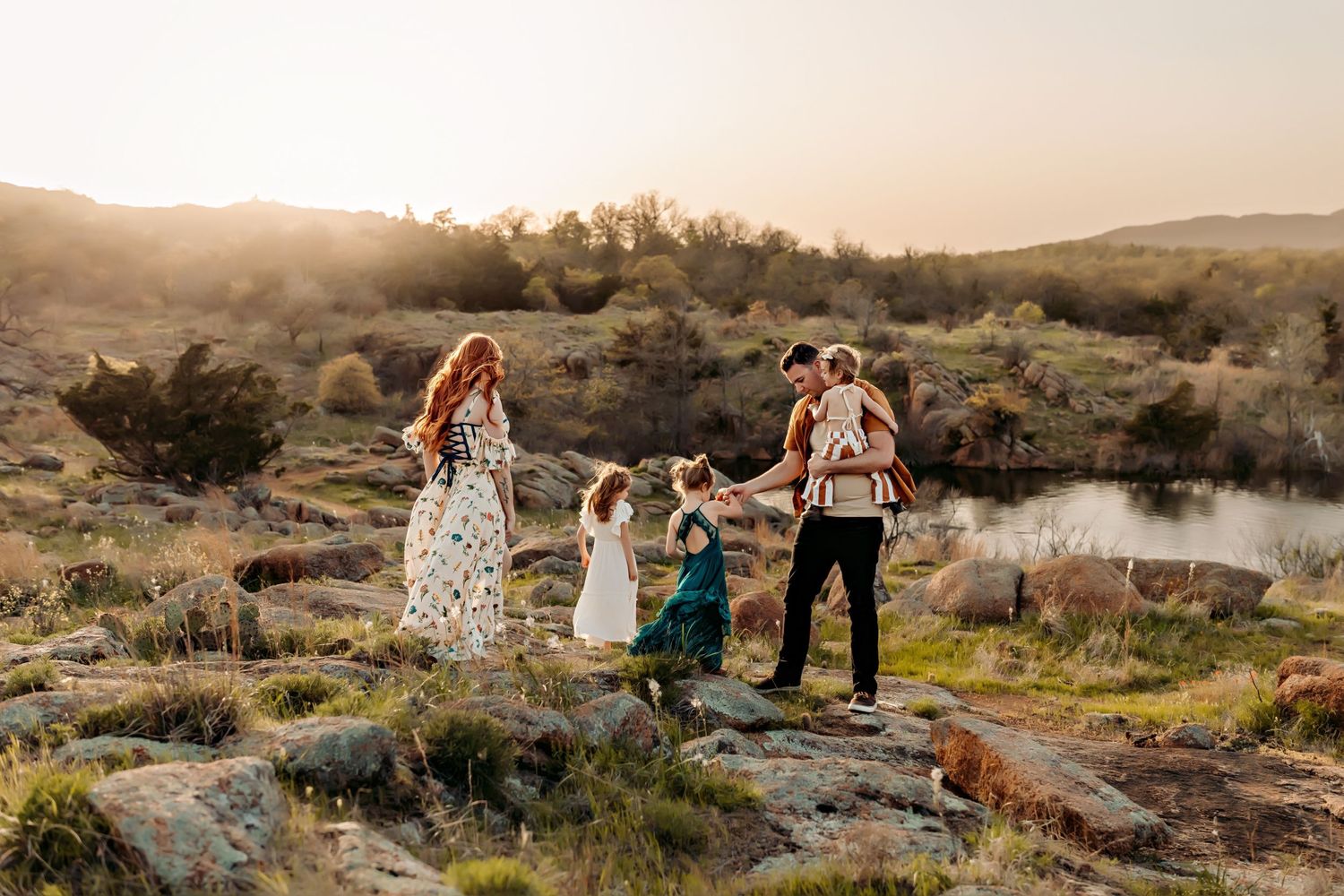 A family holds hands while standing on rocky terrain at sunset with a misty river and mountains in the background.