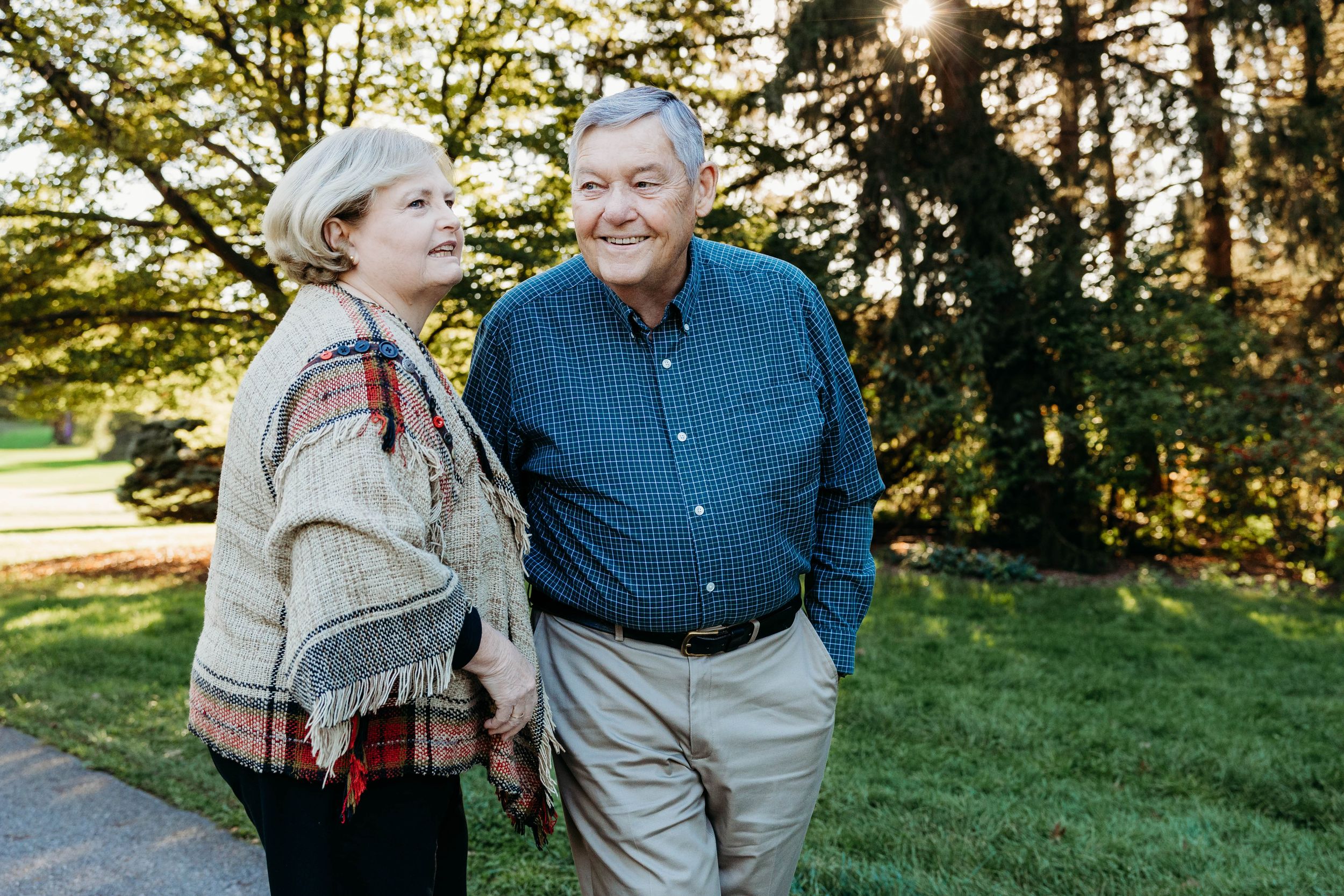 A couple laughs together on a sunny autumn day in a park with golden sunlight filtering through trees.