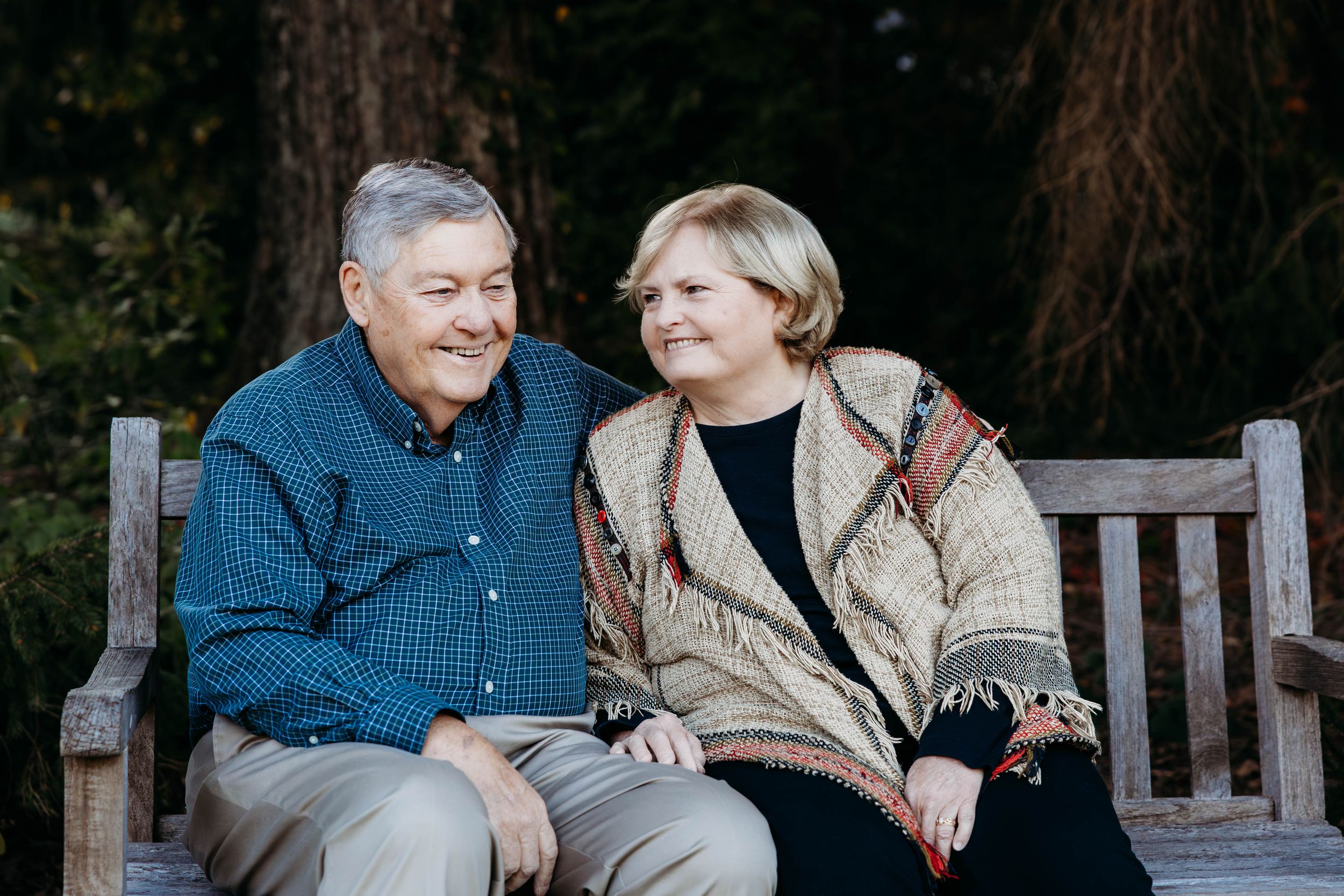 A happy senior couple sits together on a wooden bench in a garden setting, sharing a warm moment.