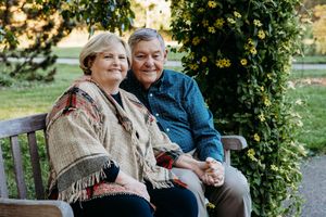 A couple sits together on a wooden bench surrounded by lush greenery in a peaceful garden setting.