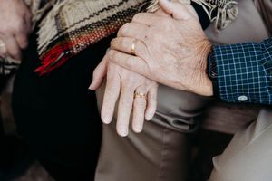 Close-up shot of hands holding each other in support and comfort against a dark background.