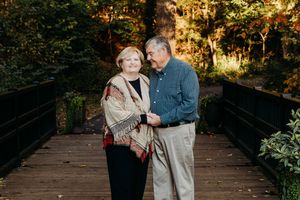 A couple shares a romantic moment on a wooden bridge surrounded by autumn foliage at sunset.