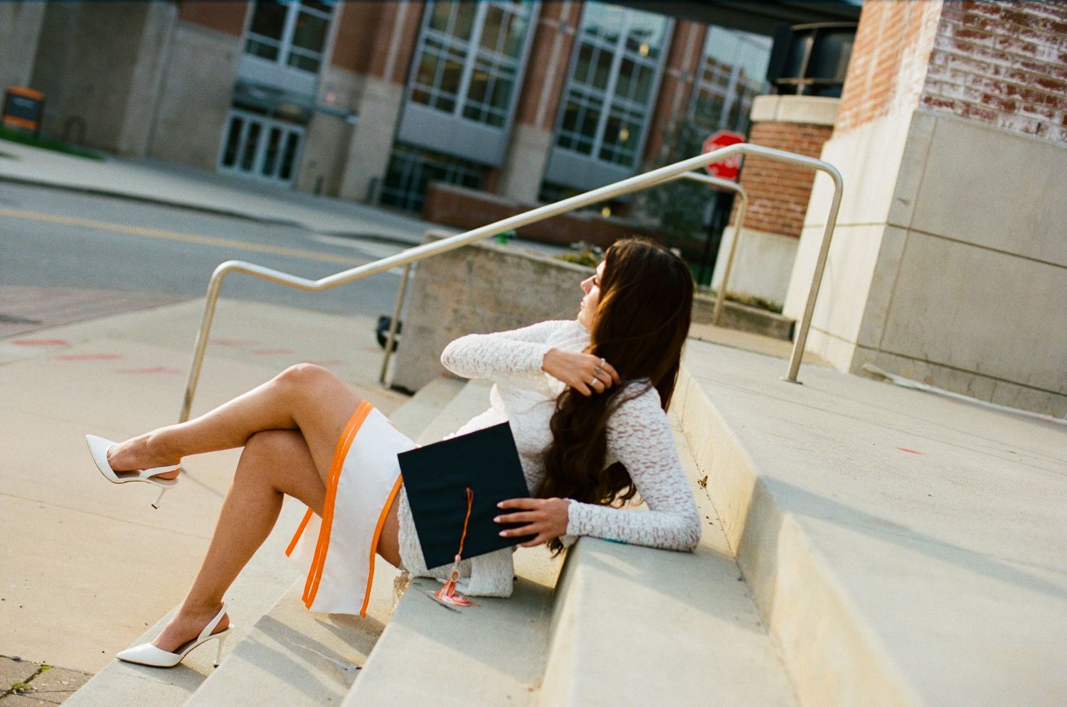 Woman in white dress reading a book while sitting on outdoor steps.