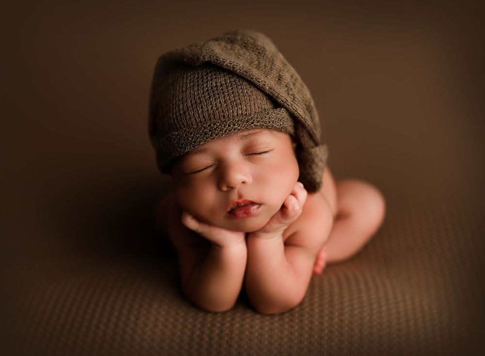Close-up artistic newborn photography with soft brown tones and knit accessories.