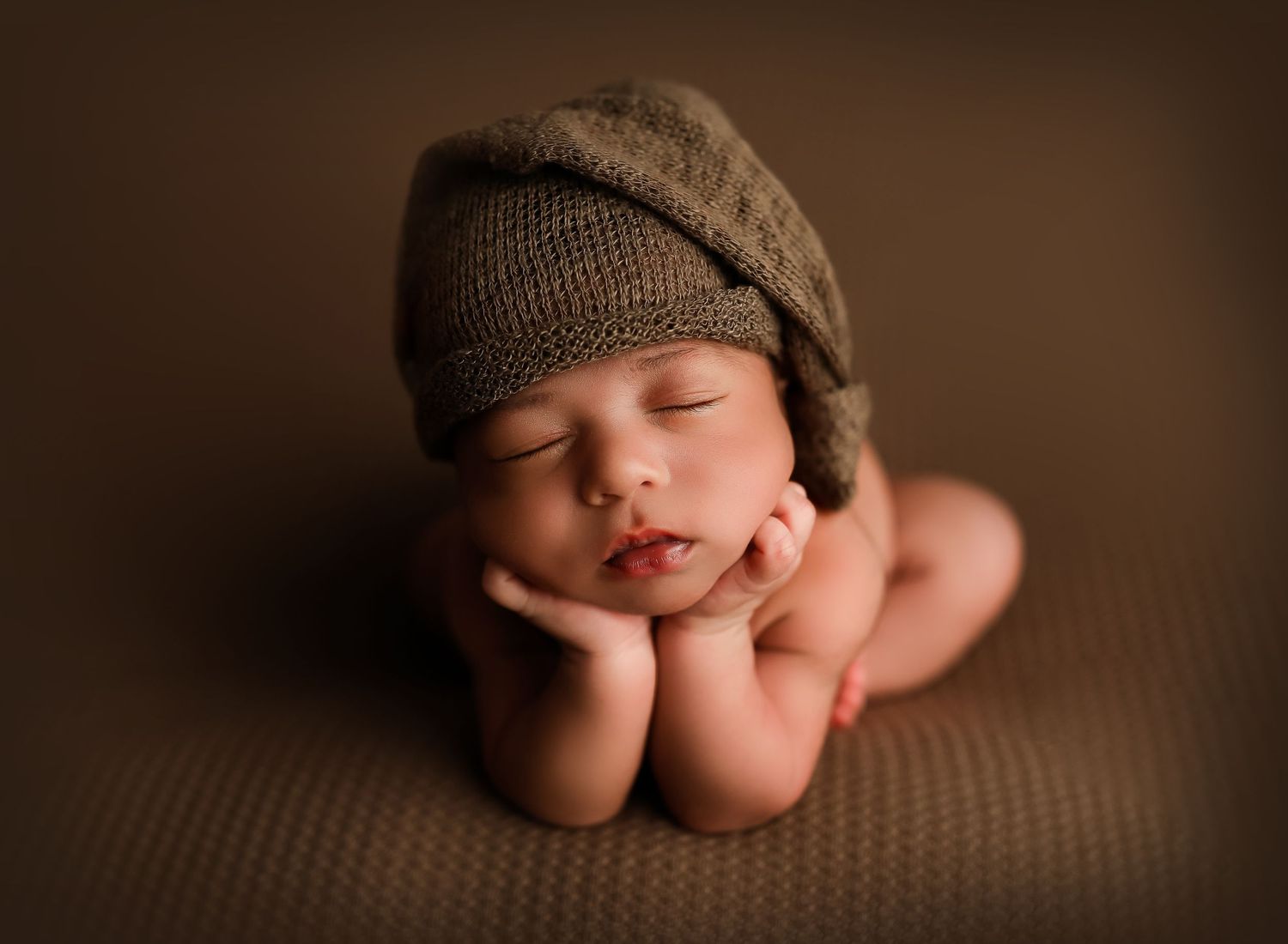Close-up artistic newborn photography with soft brown tones and knit accessories.