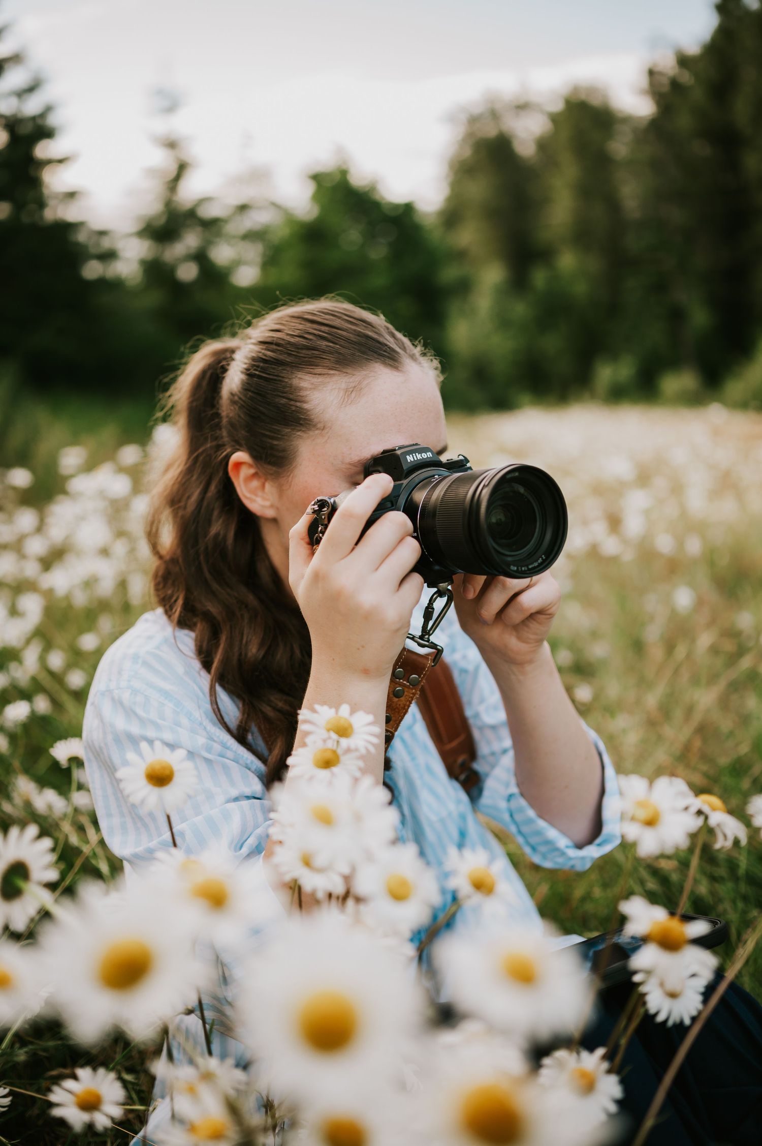 Katie the photographer in daisy field on Vancouver Island holding her camera and taking photos. Self portrait photography