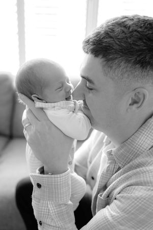 A tender black and white portrait of a parent sharing a close moment with their newborn baby in soft window light.