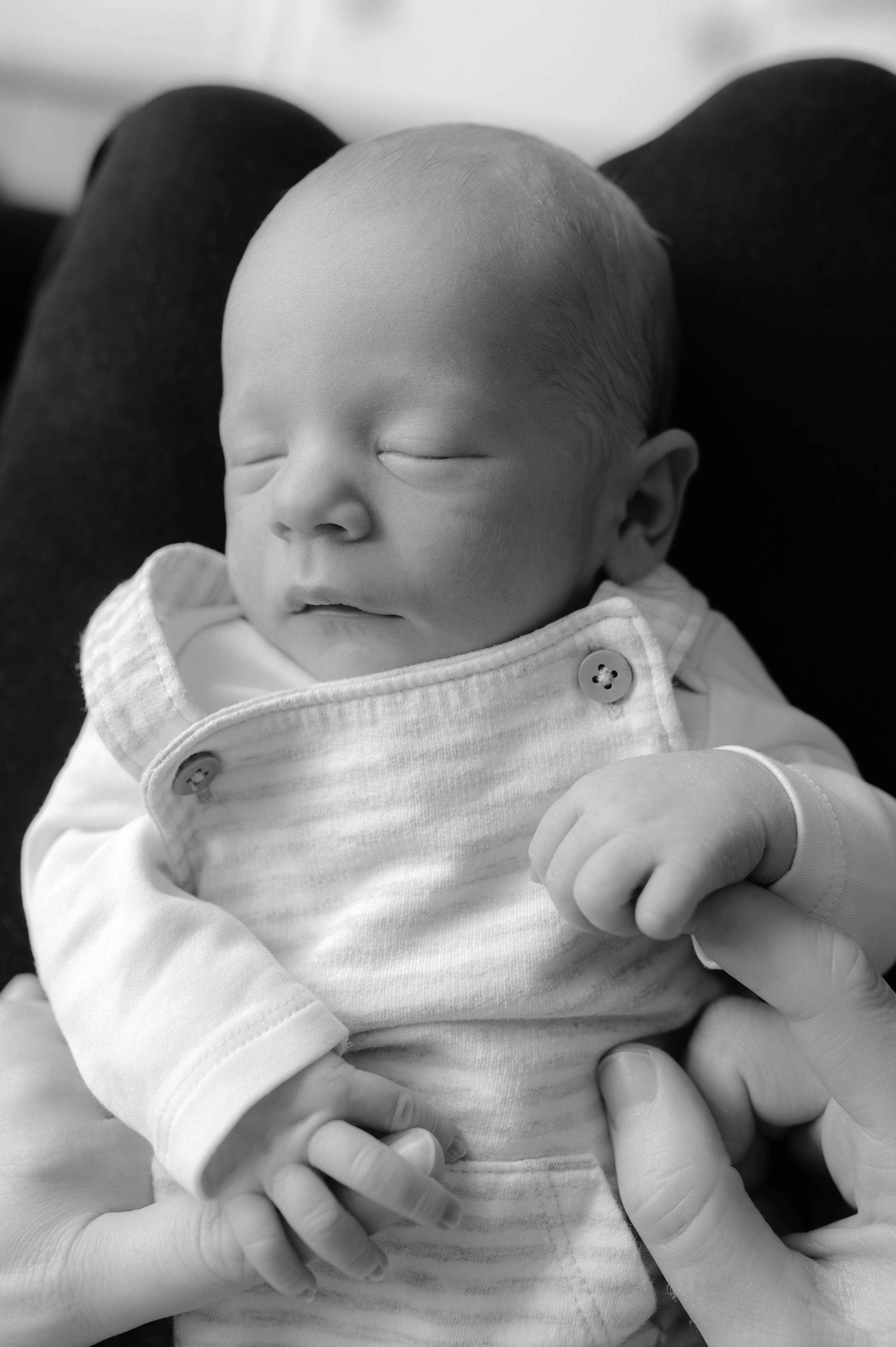 A sleeping newborn baby wearing white clothing is captured in a black and white photo series.