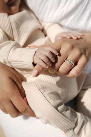 Close-up view of hands wearing a white knit sweater and delicate ring in soft natural lighting.
