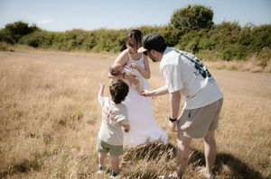 A couple in white outfits shares a tender moment together in a sunlit grassy field.