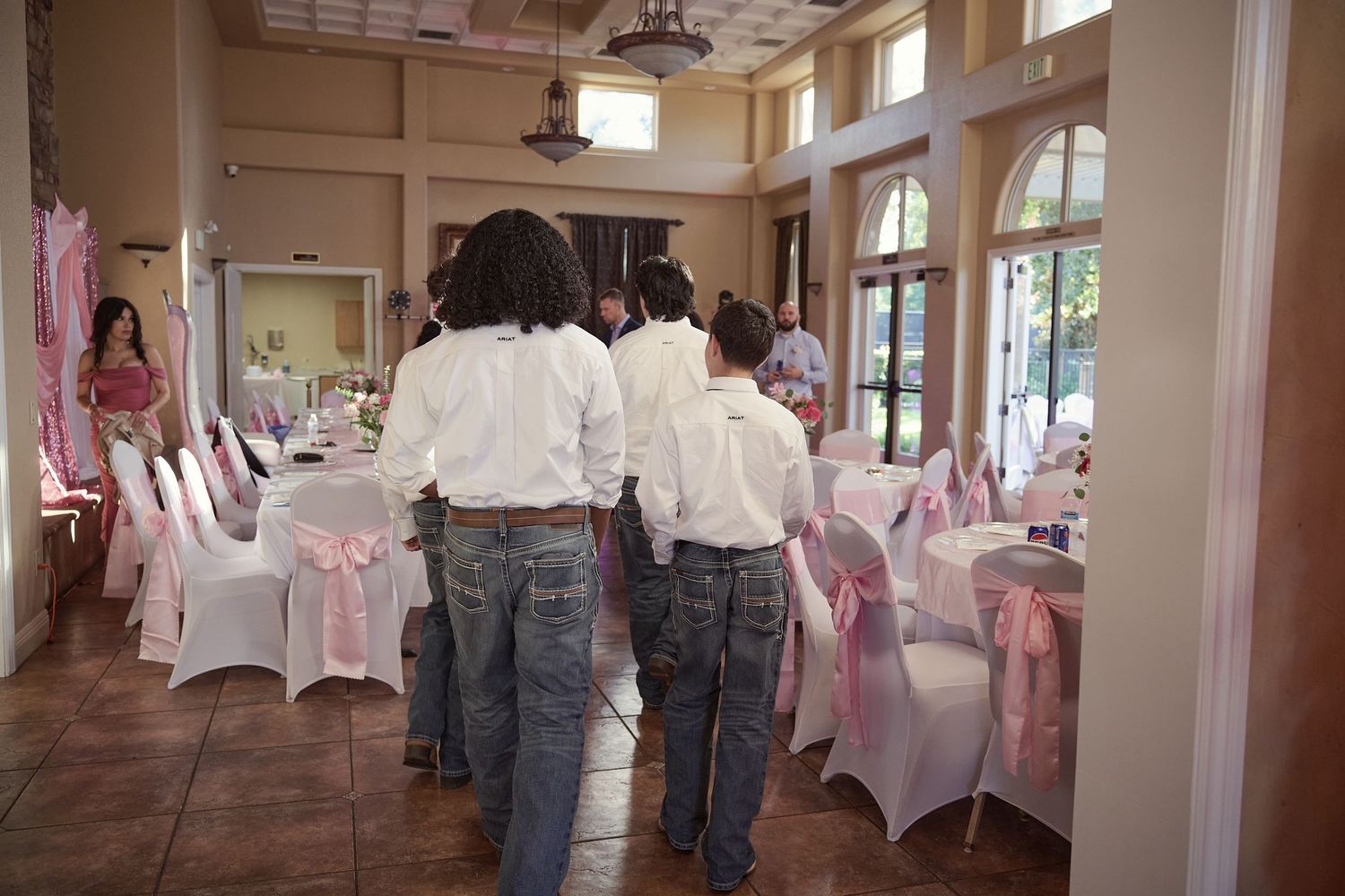 Wedding reception venue decorated with white chair covers and pink accents in a bright, airy hall.