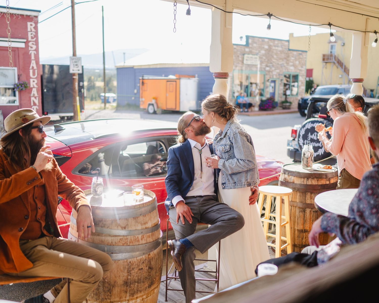 People gather around rustic wooden barrels at an outdoor venue during a social event in the afternoon light.