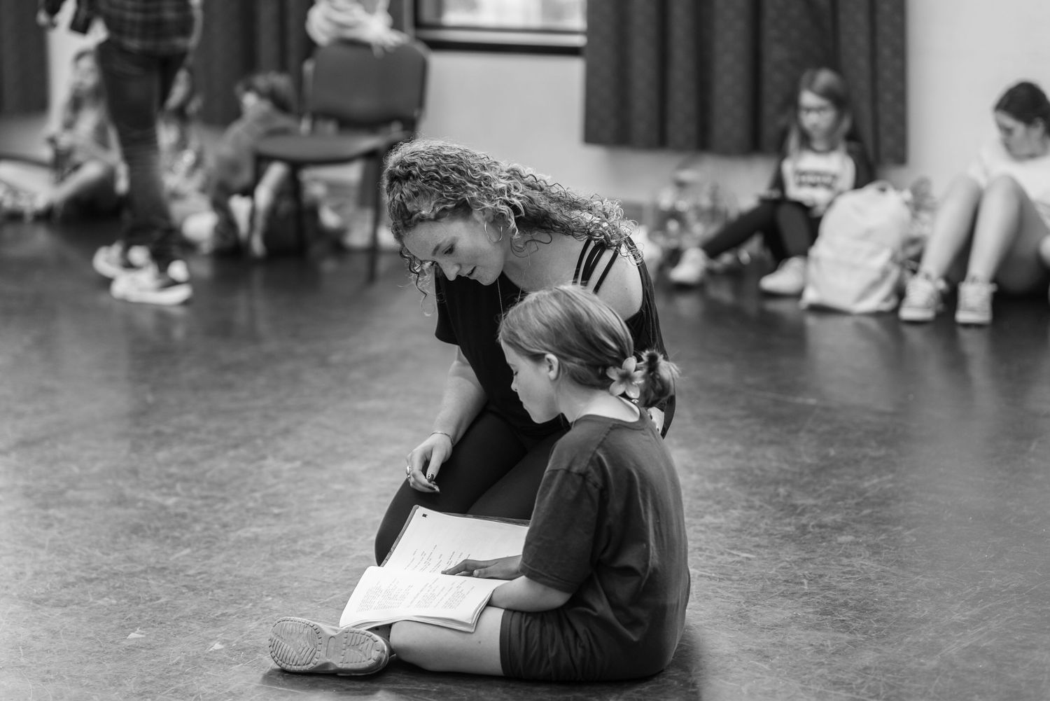 Person sitting on dark floor in rehearsal or dance studio space.