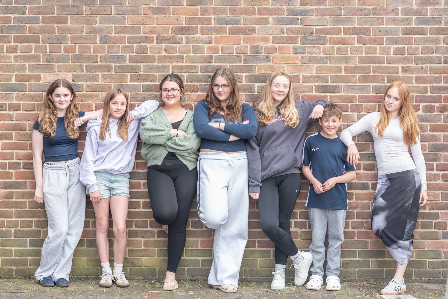 Group shot of people leaning against a brick wall wearing casual clothing.
