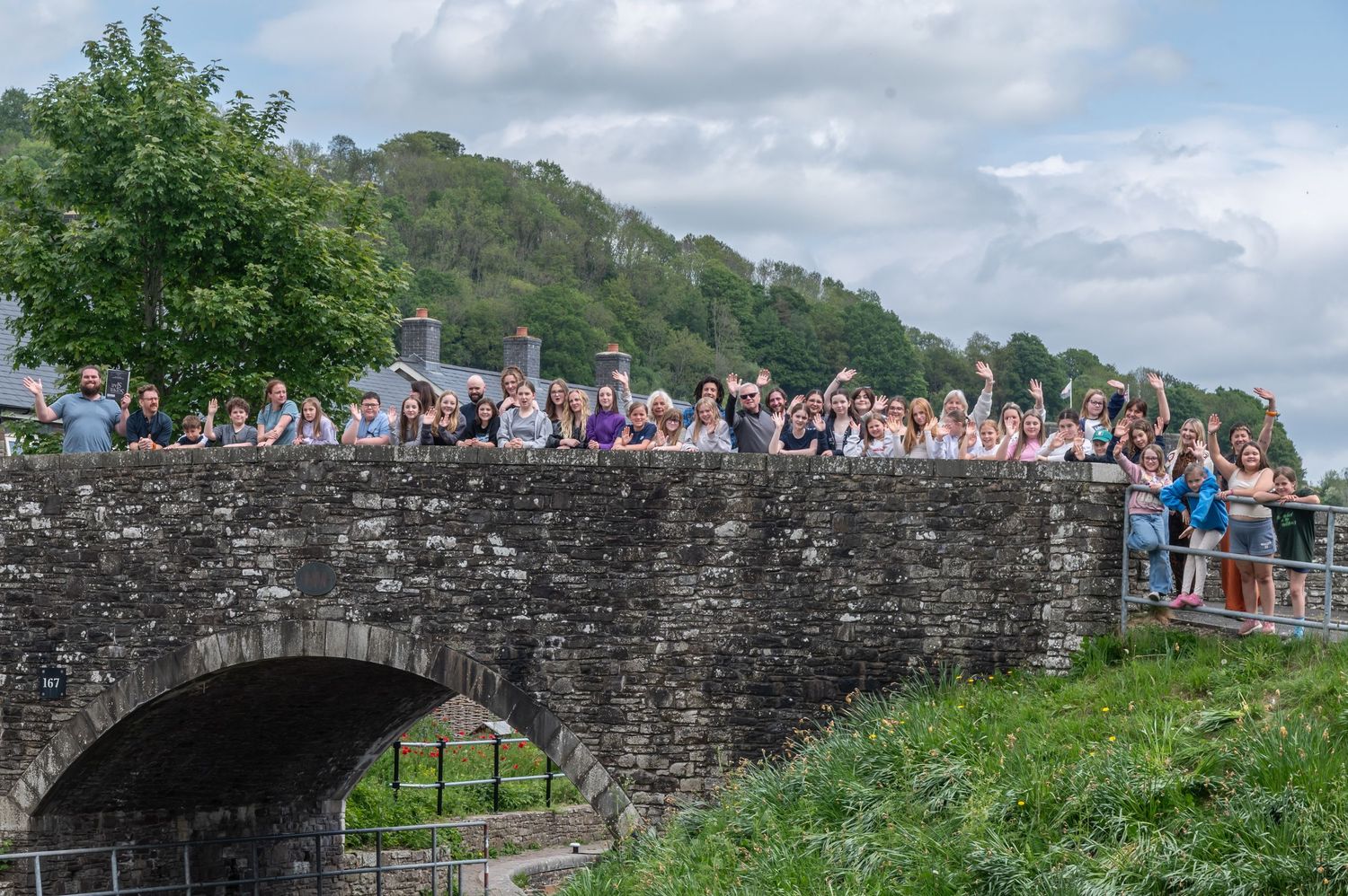 Stone bridge walkway with crowd of tourists overlooking scenic mountain landscape.