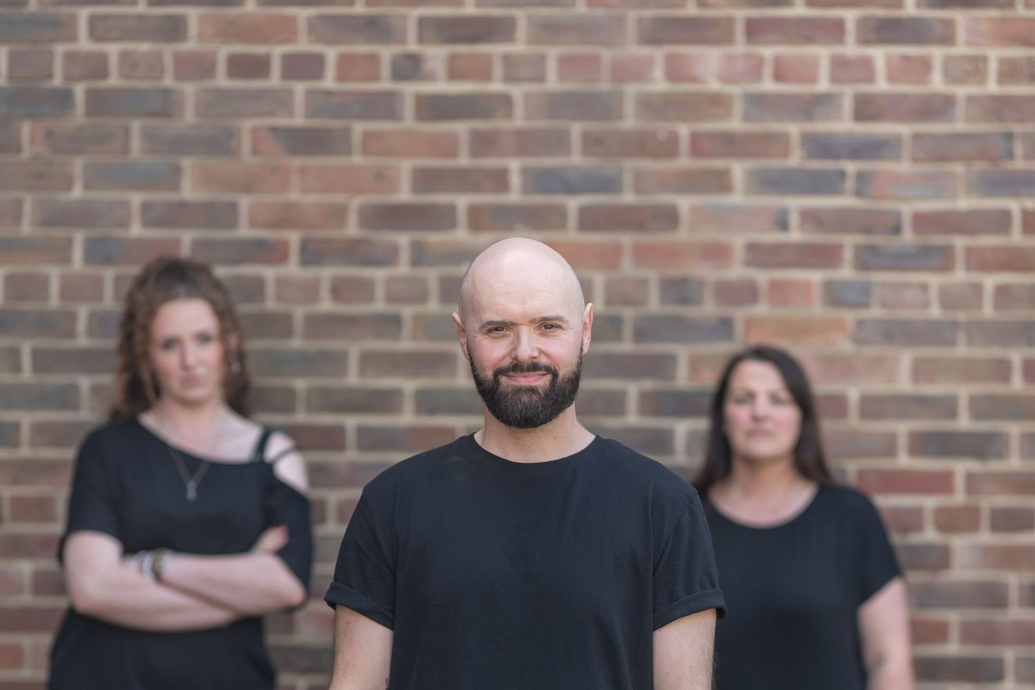 Group of performers in black attire standing against brick wall background.