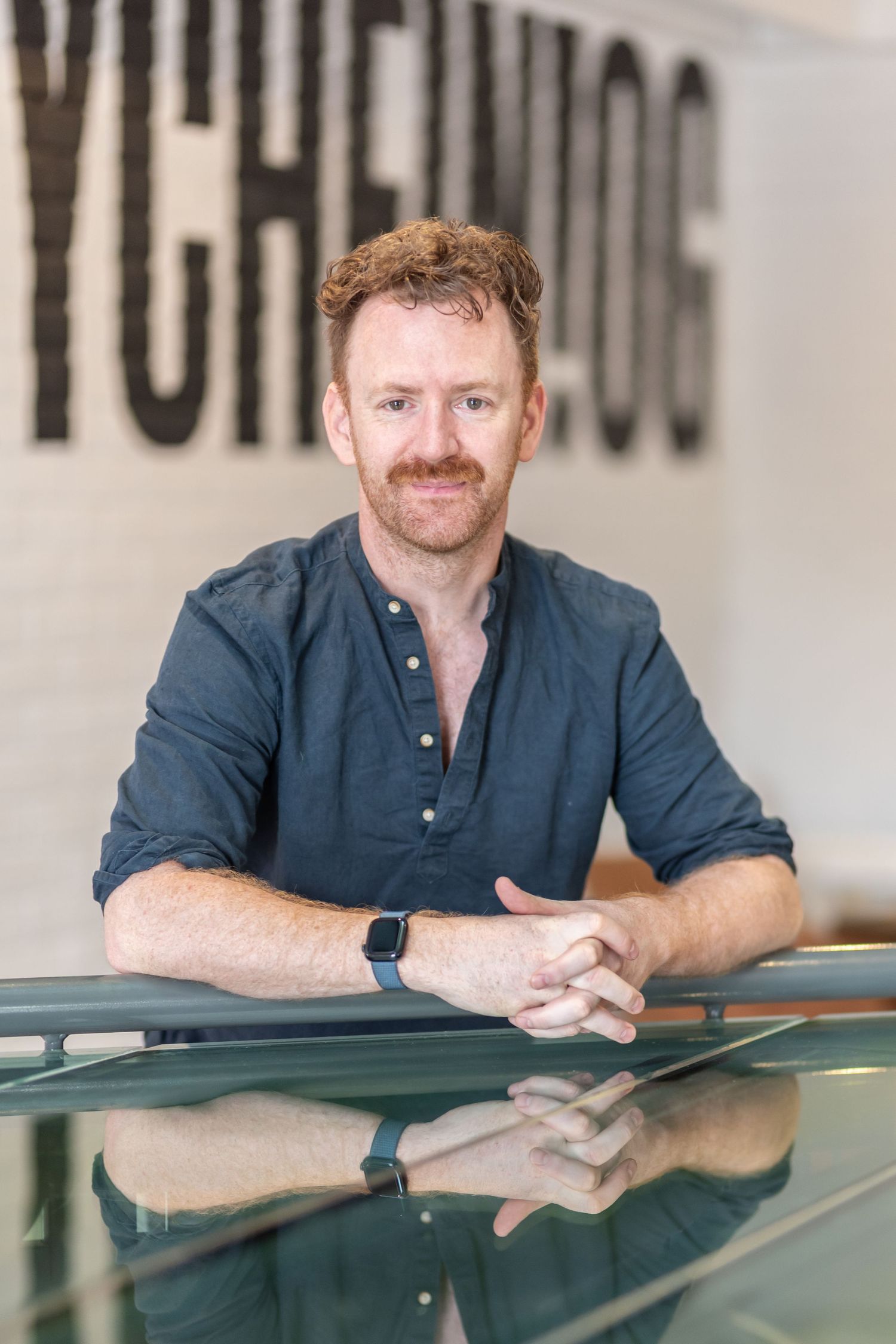 Man in navy shirt leaning on reflective surface in professional headshot series.