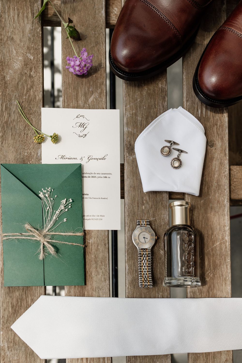 Wedding invitation and decor details including brown leather shoes and rings on rustic wooden background.