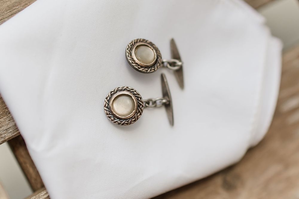 Close-up of elegant pearl and silver cufflinks with intricate circular design lying on white fabric.