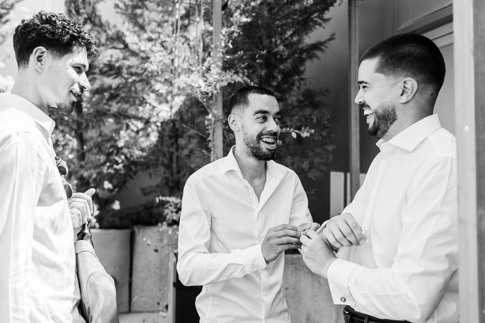 Three friends in white button-down shirts having an animated conversation outdoors in black and white.